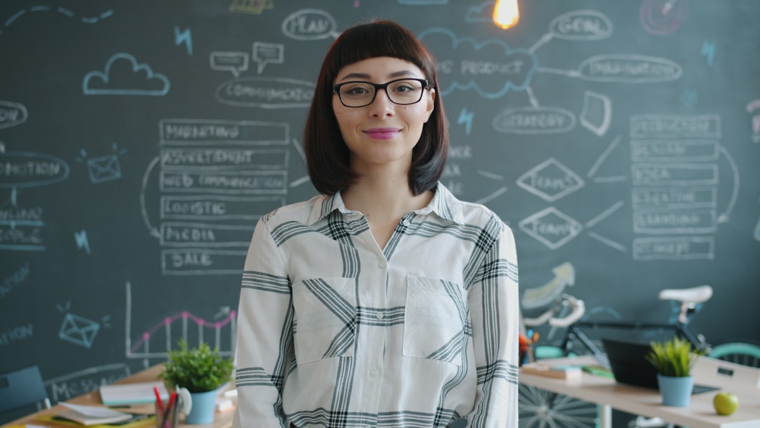 Beautiful young woman office worker standing indoors in workplace smiling and looking at camera with cheerful face. People, occupation and emotions concept.